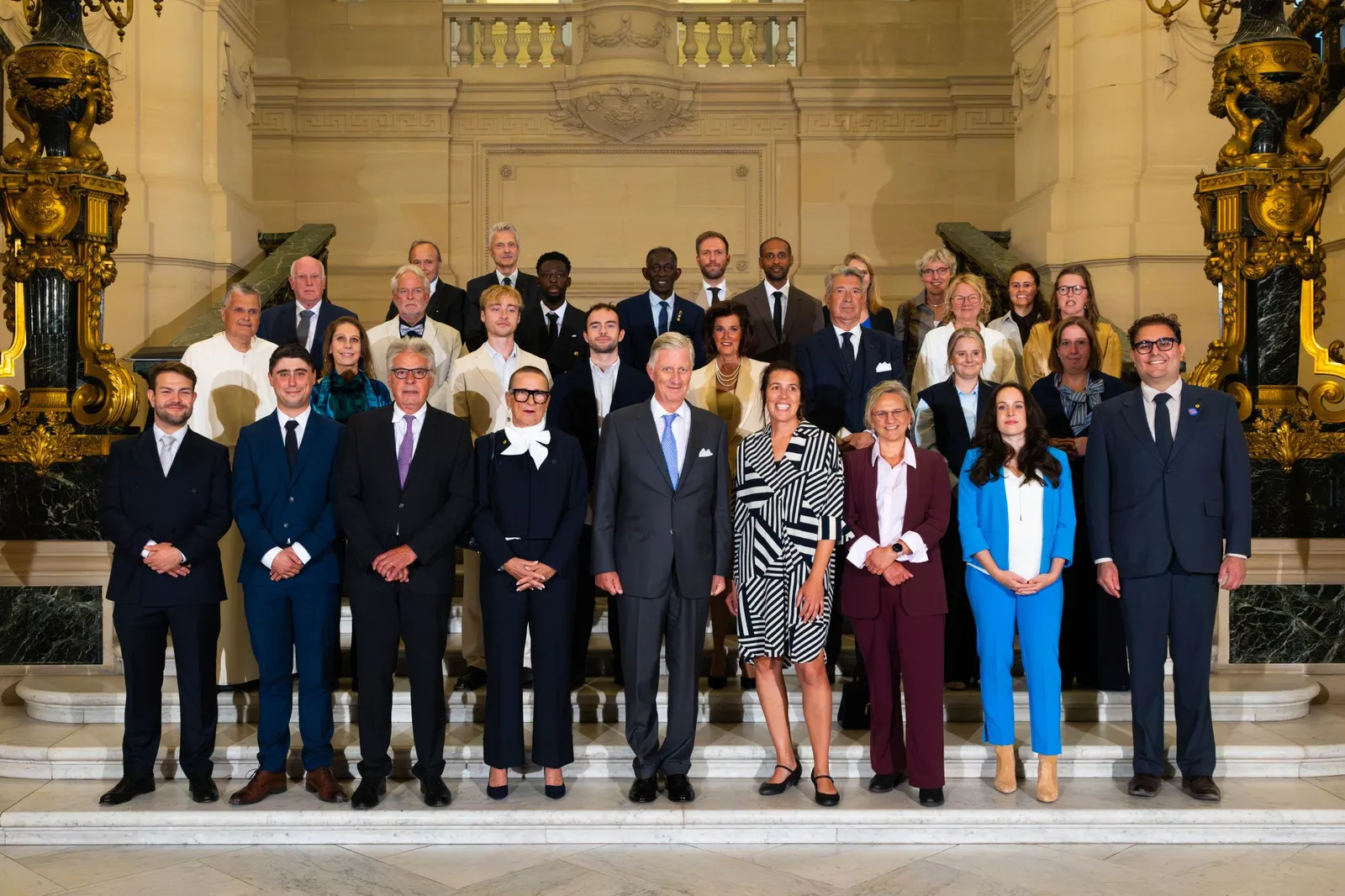 Photo de groupe des douze BeHeroes avec le roi Philippe dans l'escalier du Palais royal