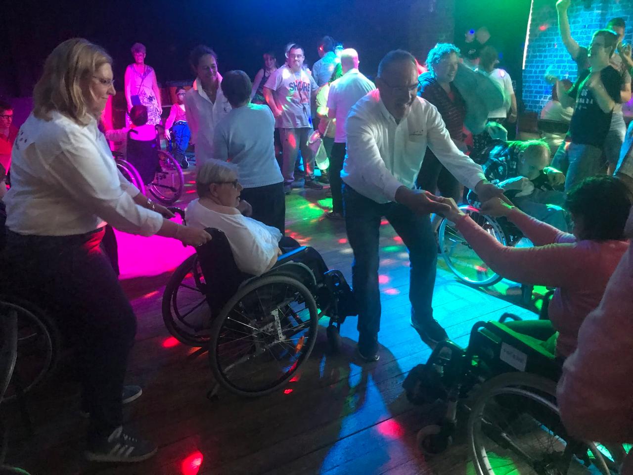 Invités et bénévoles dansent ensemble, avec et sans fauteuil roulant.