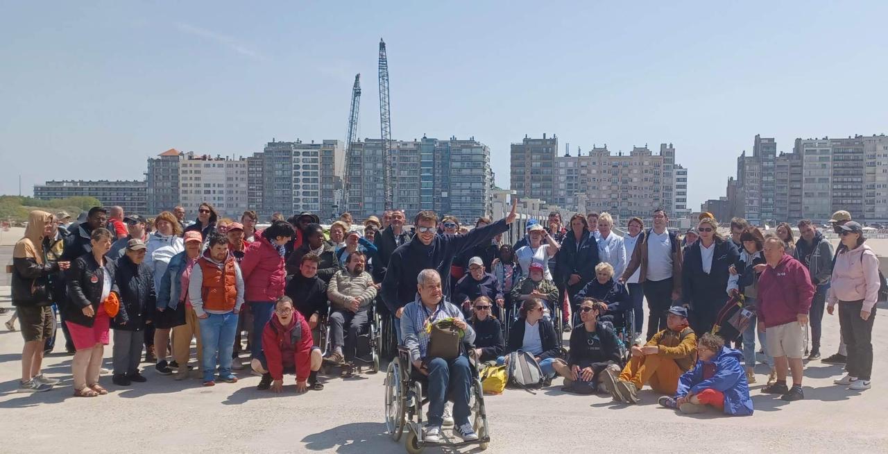 Le groupe pose près de la mer, des immeubles à l’arrière-plan.