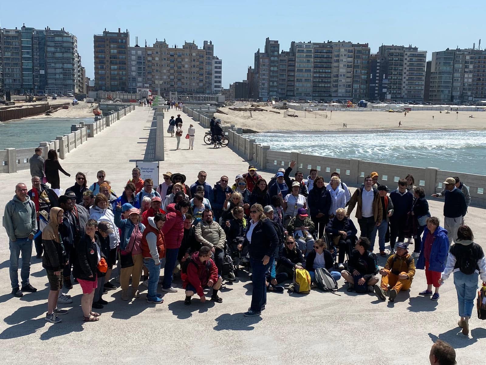 Le groupe pose sur une plage, devant une digue et des immeubles.